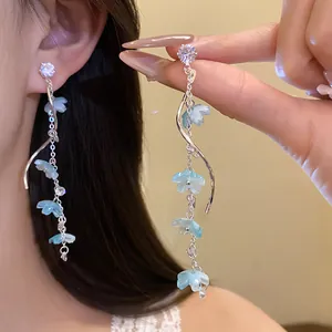 Close-up of long silver tassel earrings featuring light blue flowers and sparkling zircons.