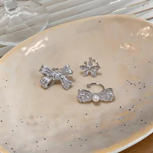 Detailed view of three silver zircon ear cuffs in bow and flower shapes on a ceramic plate.