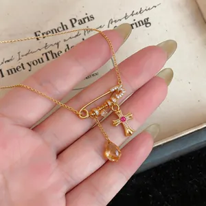 Close-up of 18k gold plated safety pin necklace with zircon cross and amber drop