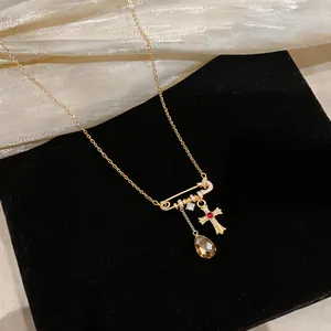 Close-up of 18k gold plated safety pin necklace with zircon cross and teardrop charms