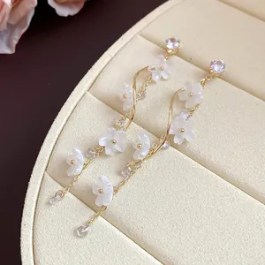 Detail view of elegant long tassel earrings with white matte flowers and sparkling zircon.