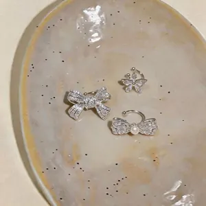 Detailed view of sparkly zircon bow and butterfly ear cuffs on a ceramic plate