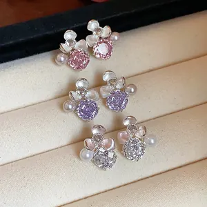 Close-up of floral zircon and pearl stud earrings in pink, purple, and clear