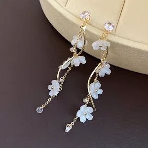 Close-up of elegant gold tassel earrings with zircon studs and white flower petals