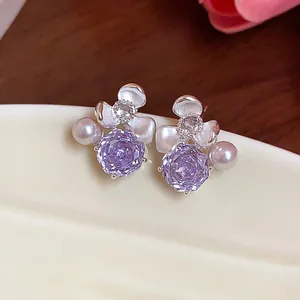 Detailed macro view of elegant purple zircon and pearl flower stud earrings on ceramic dish