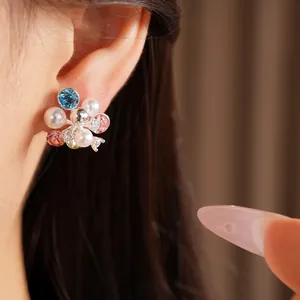 Close-up of elegant flower cluster stud earrings with pearls and colorful crystals on ear