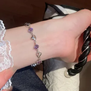 Detail view of a silver heart bracelet with sparkling purple crystals on a female wrist.