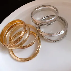 Vista macro di vari bracciali in metallo oro e argento con trame su un piatto bianco.