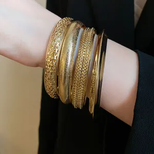 Bracciali rigidi in metallo dorato testurizzato impilati sul polso su sfondo nero chic.