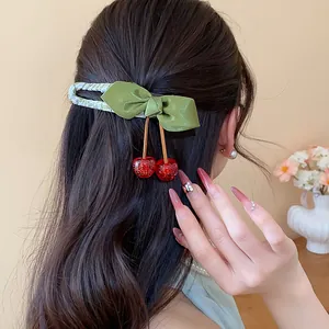 Close-up of green bow hair clip with dangling red resin cherries on dark wavy hair