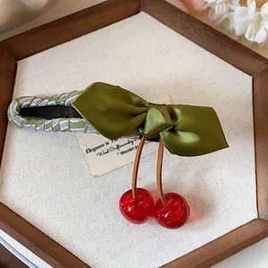 Detail of elegant green fabric bow hair clip with red resin cherries