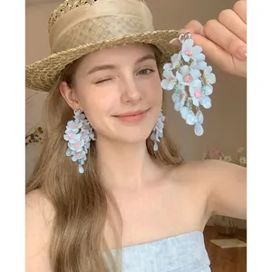 Detailed view of blue fabric flower tassel earrings worn by a model in a summer hat.