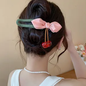 Detailed macro view of a pink satin bow hair clip with dangling red resin cherries