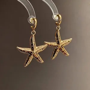 Elegant gold starfish drop earrings featuring vintage textured finish on dark background
