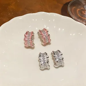 Elegant C-shaped pleated earrings with zirconia and pink enamel accents on a white plate.