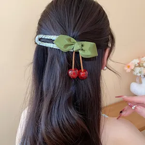 Macro detail of a green cloth bow hair clip with red resin cherries in long dark hair