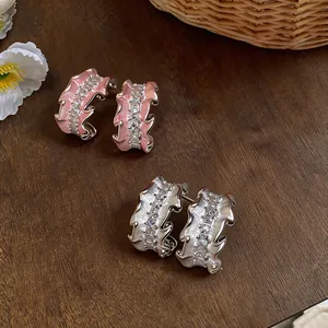 Close-up detail of pink enamel and silver pleated C-shaped earrings with inlaid zircons