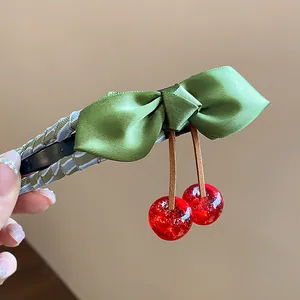 Detailed close-up of green silk bow and shiny red resin cherry charms on a hair clip.
