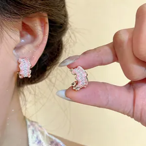 Close-up detail showing pink enamel pleated C-shaped earrings with sparkling cubic zircons