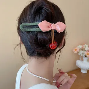 Close-up detail of a stylish pink bow hair clip with red cherry charms on a bun hairstyle