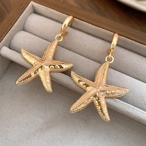 Detailed macro view of golden starfish drop earrings in a grey velvet jewelry box