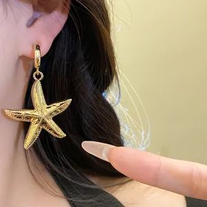 Close-up of a textured gold starfish pendant earring worn on a model's ear.