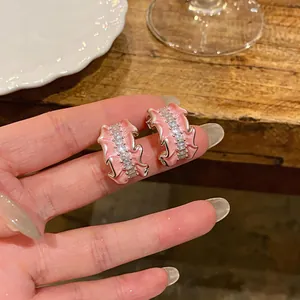 Close-up of light pink pleated enamel C-shaped earrings with clear zircon stones.