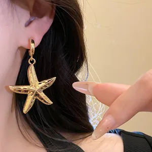 Close-up detail of a textured gold starfish drop earring showing intricate metal finish