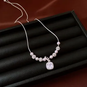 Macro detail of a silver necklace with square zircon pendant and pearls on black display.