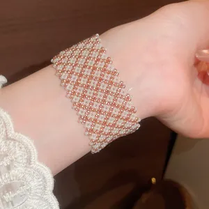 Dettaglio del bracciale largo in perline di vetro a scacchi rosa e bianchi indossato al polso