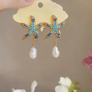 Close-up of elegant gold starfish stud earrings with blue rhinestones and baroque pearls