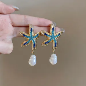 Macro shot of summer style gold starfish earrings with blue rhinestones and pearls