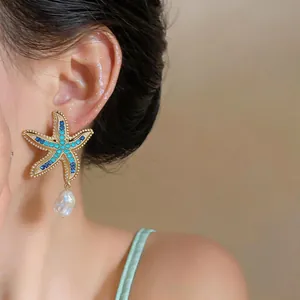 Close-up of a stylish starfish earring with blue crystals and a pearl drop on a model