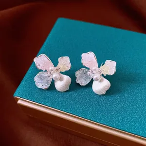 Elegantes pendientes de flores y perlas en un joyero verde azulado.