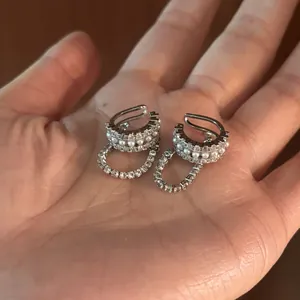 Primo piano di ear cuff asimmetrici in argento con perle e zirconi sulla mano.