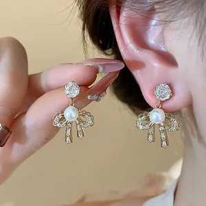 Close-up of elegant bow earrings featuring a pearl center and sparkling zircon accents in gold