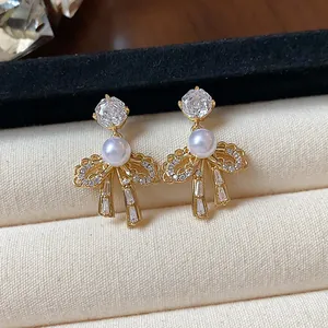 Close-up of elegant 18k gold plated bow earrings with pearls and sparkling zircons.