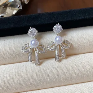 Macro detail of bow-knot earrings featuring elegant pearl and shimmering zircon.