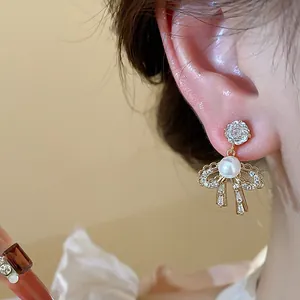Close-up detail of a bow-knot earring with pearl and zircons on an ear.
