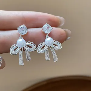 Close-up of elegant bow stud earrings with white pearl and sparkling zircon details