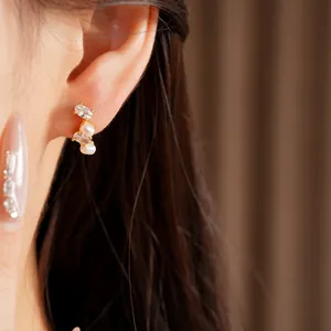 Dettaglio di orecchini a perno minimalisti in argento dorato con perle e zirconi
