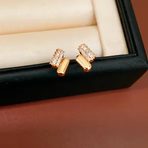 Primo piano di orecchini dorati minimalisti con pavé di zirconi e finitura lucida.