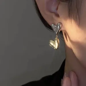 Detailed close-up of double heart drop earrings in silver and gold finish on model's ear