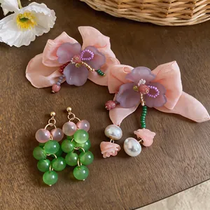 Detailed view of chiffon flower studs and green beaded grape earrings on wood.