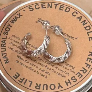 Elegant silver twisted hoop earrings with sparkling zircon stones on a rustic candle lid