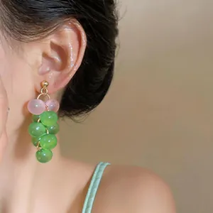 Close-up view of elegant pink and green grape-shaped glass bead earrings on a model
