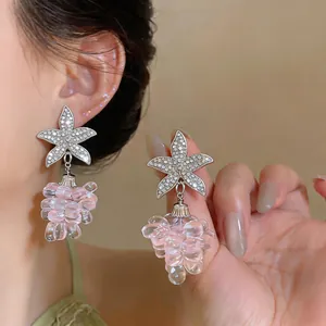 Detalle de pendientes de estrella plateada y cuentas rosas en forma de uva con cristales finos