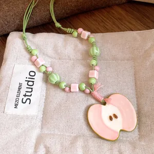 Close-up detail of a pink ceramic apple pendant necklace with fresh green and pink beads