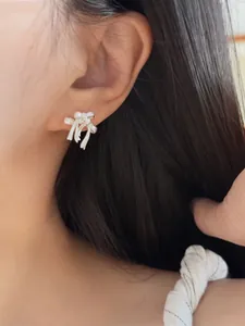 Close-up detail of a minimalist silver ribbon bow earring with zircon stones worn on ear