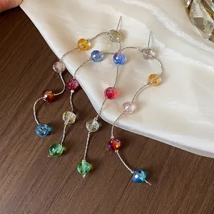 Detailed view of colorful faceted glass bead long tassel earrings on white silk fabric